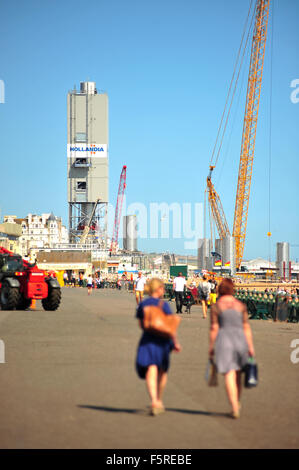 Pedestrians walk along the Brighton seafront with the i360 observation tower construction site visible in the background. Stock Photo