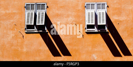 Two shuttered windows casting long shadows in the old town in Nice France Stock Photo