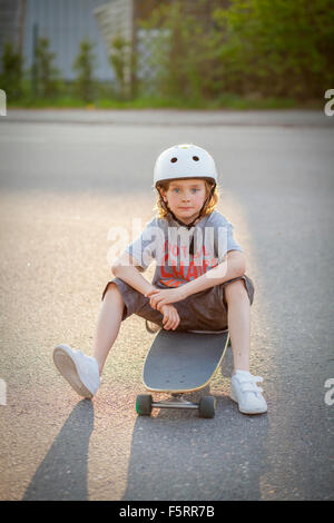 Sweden, Vastergotland, Lerum, Portrait of boy (8-9) sitting on skateboard on street