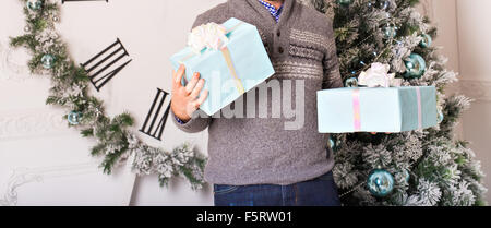 Young man holding gifts in front of Christmas tree Stock Photo