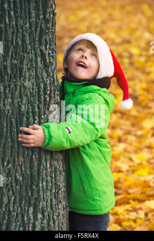 boy with Santa hat hugging a tree in park in the fall Stock Photo