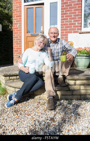 Senior Couple Sitting Outside House With Cup Of Coffee Stock Photo