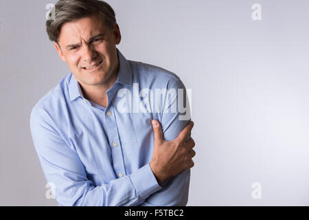 Studio Of Mature Man Clutching Arm As Warning Of Heart Attack Stock Photo