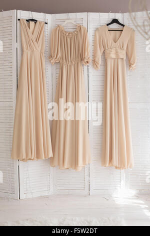 Three beige dresses for bridesmaids hang on hangers in the room Stock Photo