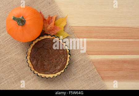Sugar pumpkin and mini pumpkin pie with autumn maple leaves on hessian and wood, with copy space Stock Photo