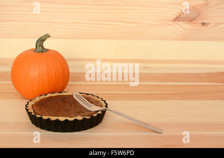 Fork with a small pumpkin pie on a wooden table with small orange gourd, with copy space Stock Photo