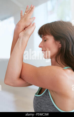 Side view of woman at gym with her crossed arms performing yoga exercise. Garudasana, Eagle pose. Stock Photo