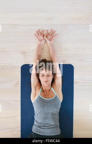 Top view of woman lying on floor with her eyes closed and stretched arms. Fitness woman exercising on yoga mat. Stock Photo