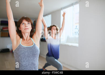 Two women practicing yoga forms and positions in gym. Fitness females doing warrior pose at yoga class. Virabhadrasana posture i Stock Photo