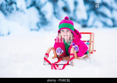 Little girl shoveling snow on home drive way. Beautiful snowy garden or front yard. Child with shovel playing outdoors in winter Stock Photo