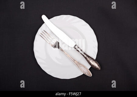 Plate, fork and knife top view on black cloth background Stock Photo