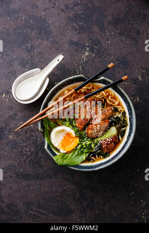 Duck noodles with egg and pak choi cabbage in bowl on dark black stone texture background Stock Photo