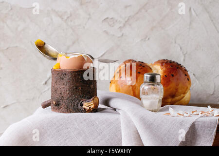 Breakfast with started eating soft-boiled egg with pouring yolk in wooden eggcup and home made bread served with salt and silver Stock Photo