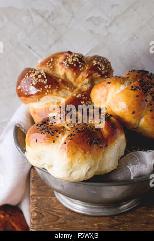 Heap of sweet round sabbath challah bread with white and black sesame seeds in vintage metal bowl on wooden table with plastered Stock Photo