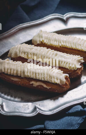 Home made Eclairs with white butter cream in vintage metal plate. Dark rustic style. Day light. Outside view Stock Photo