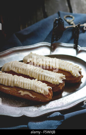 Home made Eclairs with white butter cream in vintage metal plate. Dark rustic style. Day light. Outside view Stock Photo