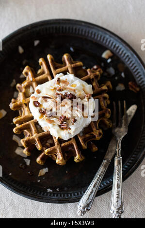 Spicy pumpkin waffles topped with coconut whipped cream, pecans, and maple syrup are photographed from top. Stock Photo