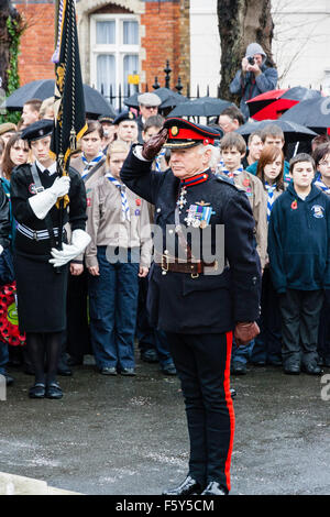 England, Ramsgate. Remembrance Day. Senior military officer saluting at war memorial during ceremony in the rain. Background boy scouts standing. Stock Photo