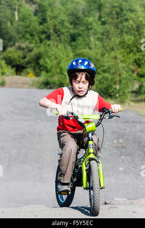 Caucasian child, 9 year old boy, riding child's bike towards viewer on dirty track, while wearing a crash helmet. Full length. Sunshine. Stock Photo