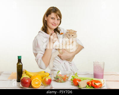 Young beautiful girl in a bathrobe prepares vegetarian salad from vegetables and greens isolated on white background Stock Photo