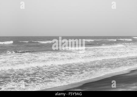 Incoming frothy sea waves on a tropical beach. These rushing waves leave curved patterns on the beach. Black and white image. Stock Photo