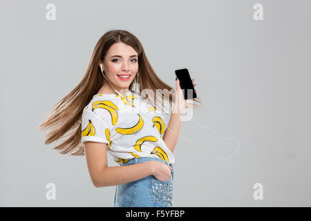Portrait of a smiling woman with headphones showing blank smartphone screen isolated on a white background Stock Photo