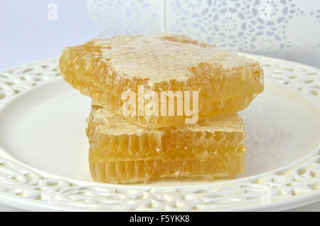 Appetizing pieces of fresh honeycomb on fine porcelain plate with lacy metallic structure in background Stock Photo