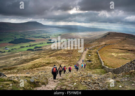 Walkers descend the path from Whernside, in the Yorkshire Dales National Park, with a view of Ingleborough hill on the horizon. Stock Photo
