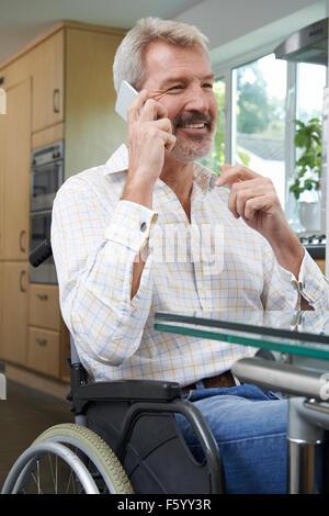 Disabled Man In Wheelchair Making Call On Mobile Phone At Home Stock Photo