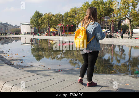 Woman standing in front of reflection of trees on the water at Museumplein, Rijksmuseum in Amsterdam, the Netherlands. Stock Photo