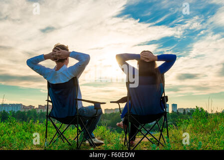 couple sitting in chairs and admire the sunrise over the city Stock Photo