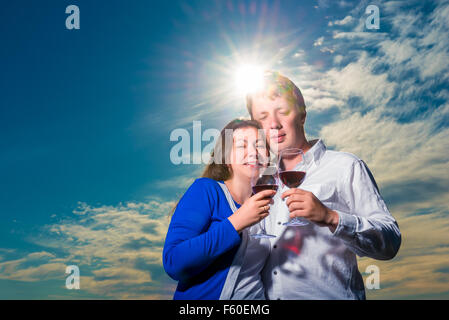 couple with glasses of wine embraces under the rays of the setting sun Stock Photo