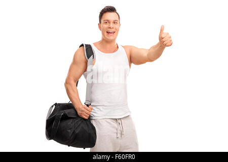 Muscular young man carrying a black sports bag and giving a thumb up isolated on white background Stock Photo