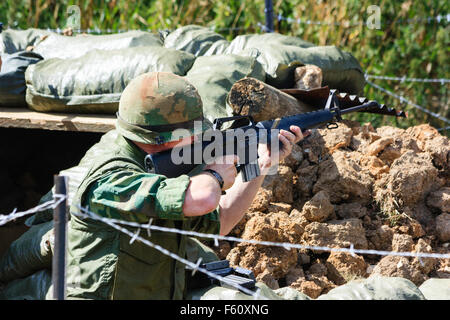 Vietnam war re-enactment. Close up of American Marine firing M16 from entrenched position during mock firefight. Casings being ejected from gun. Stock Photo