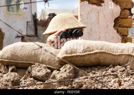 Second world war North Africa re-enactment. British 8th army soldier looking through binoculars over the top of sandbags. Close up. Stock Photo