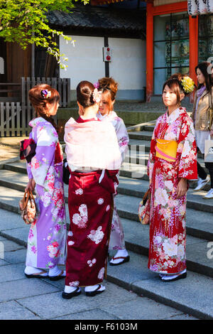 Four young Japanese women wearing kinomo standing chatting to each other on the steps of the entrance to the Yasaka Shrine in Kyoto in the springtime. Stock Photo