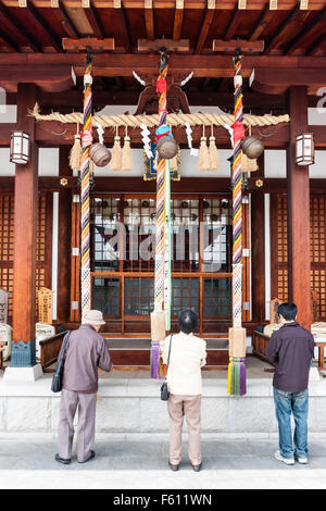 Japan, Nishinomiya, Shotaizan Tokoji temple, Three people, seen from behind, standing in line praying at main hall, each in front of bell rope. Stock Photo