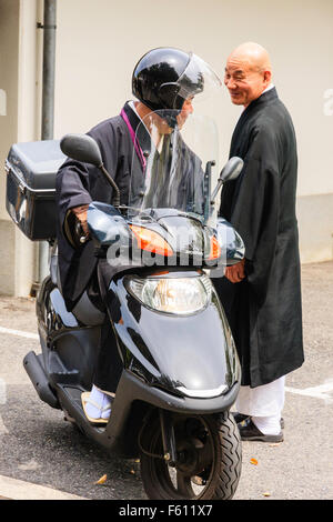 Japan, Nishinomiya, Mondo Yakuji, Shotaizan Tokoji temple, Buddhist priest in robes on motor scooter talking to another monk standing next to him. Stock Photo