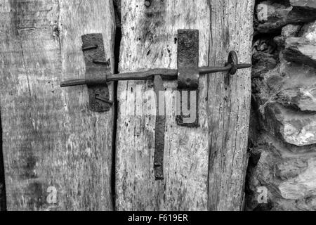 Old iron latch catch on wooden door with stone wall Stock Photo