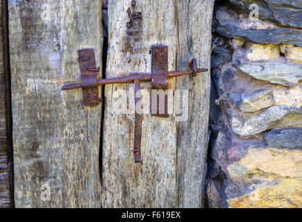 Old iron latch catch on wooden door with stone wall Stock Photo