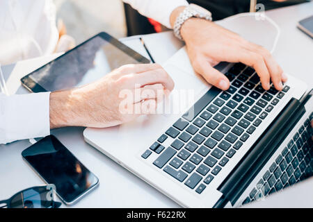 Close up on the hands of a young handsome businessman using technological devices like notebook, smartphone and tablet - communication, business, working concept Stock Photo