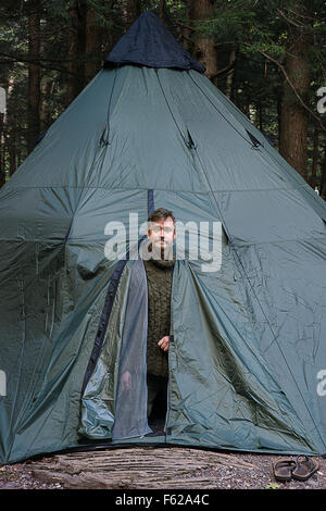 A man poking his head out of a tent shaped like a teepee. Stock Photo
