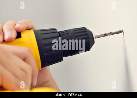 closeup of a young caucasian man boring a hole in a wall with a drill Stock Photo