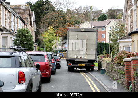 A lorry is forced to drive on the pavement or mount the kerb to pass parked cars on a narrow British street. The road is in a residential area Stock Photo