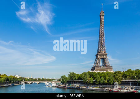 Eiffel Tower against a blue sky, with wispy clouds. In the foreground are boats on the river Seine. Stock Photo