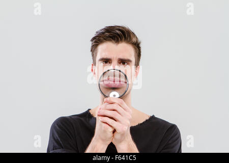 Funny handsome positive man playing tricks using magnifying glass Stock Photo