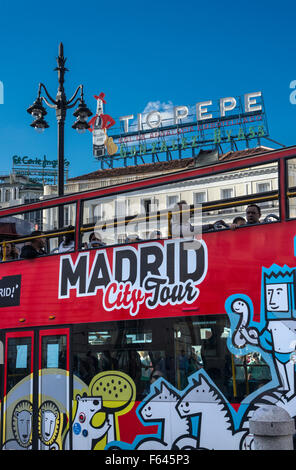 A Madrid city tour bus passes below the Tio Pepe advertising sign  in the Puerta del Sol,  Madrid, Spain. Stock Photo