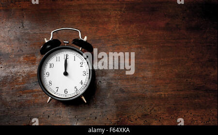 Classic old black alarm clock noon time on wooden scraped table Stock Photo