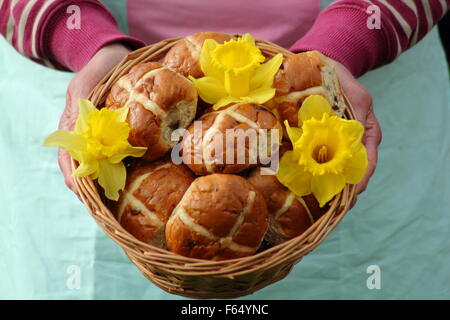A woman presents hot cross buns decorated with daffodils in a rustic wicker basket for Easter festivities in north England, UK Stock Photo