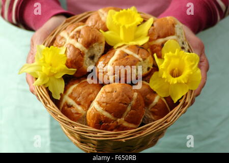A woman presents hot cross buns decorated with daffodils in a rustic wicker basket for Easter festivities in north England, UK Stock Photo